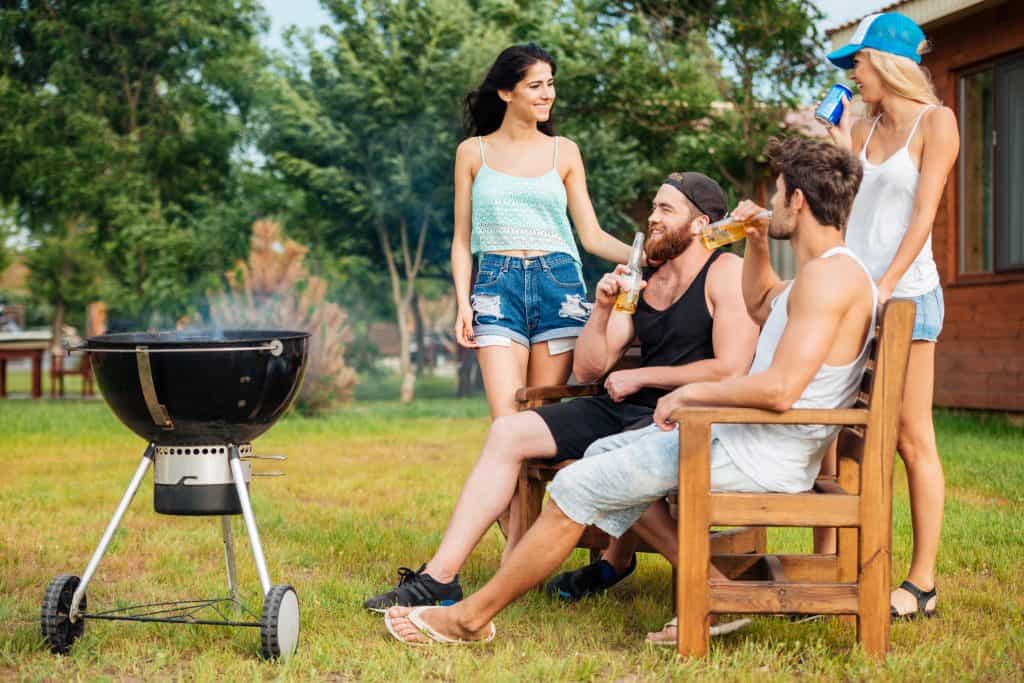 Group of young teenagers chatting while preparing barbecue grill in park zone