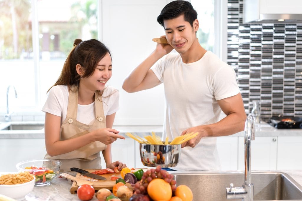 Young asian woman cutting slice vegetables making salad healthy food with fruits and man cooking menu for dinner in kitchen at home fun couple together romantic