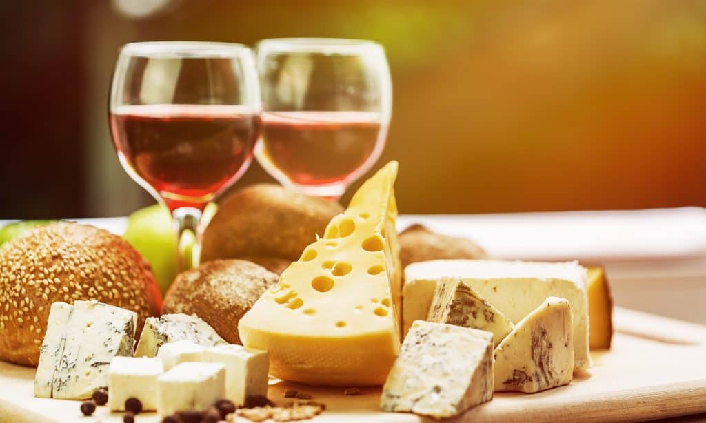 Assortment of cheese on board and two glasses of wine