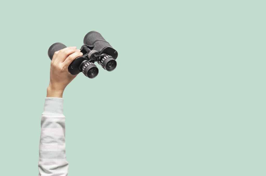 Woman with binoculars on green background, looking through binoculars, journey, find and search concept.
