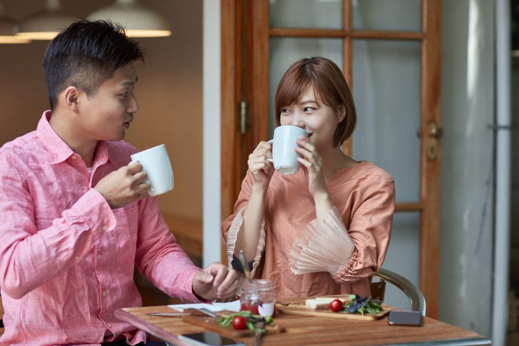 Affectionate man and woman drinking coffee at cafe. Heterosexual couple is looking each other face to face at table. They are in love.