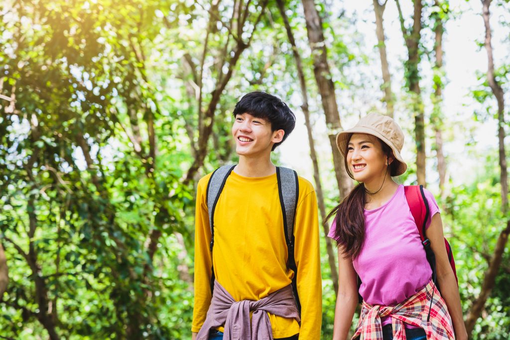 Young Asian couple hikers with backpacks enjoying walking in the forest