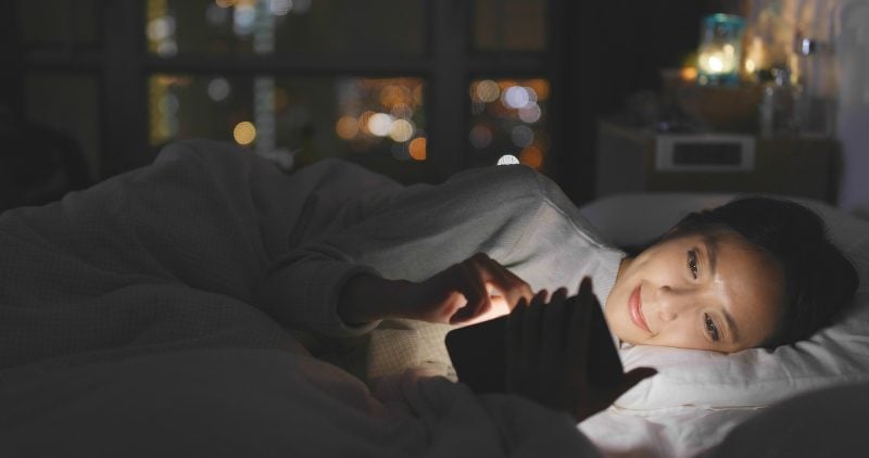 Woman use of cellphone and lying on bed at night