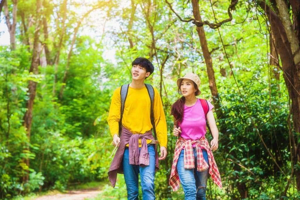 Young Asian couple hikers with backpacks enjoying walking in the forest