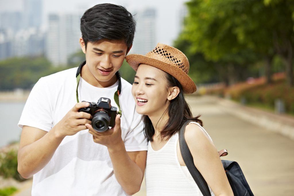 young asian couple tourists looking at camera's monitor checking pictures taken